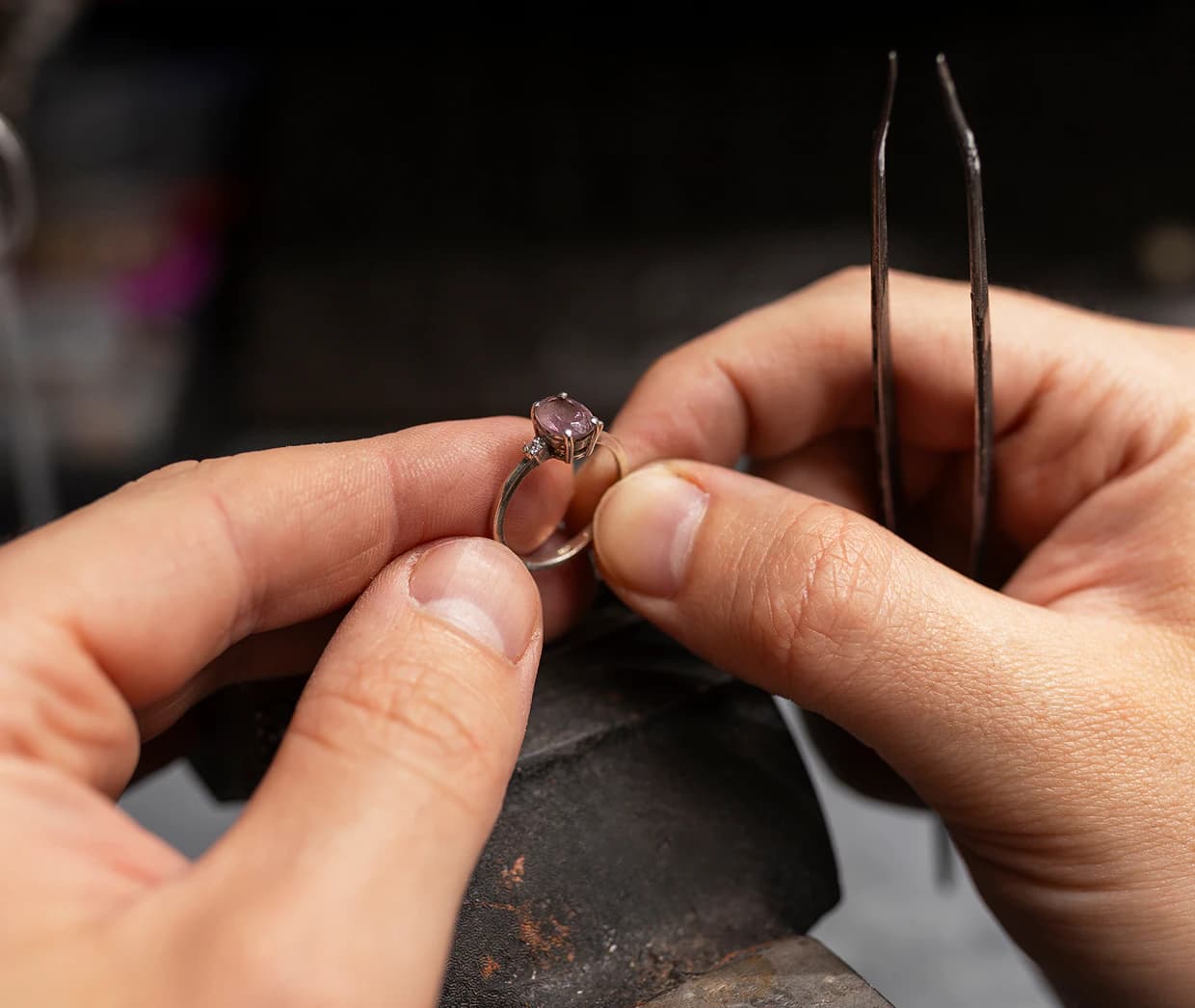 Jeweler inspecting a gemstone ring with tweezers at the workbench